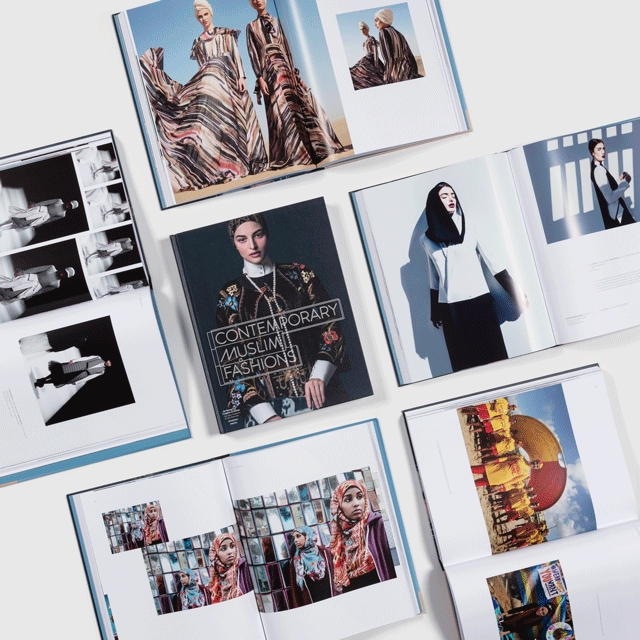 As seen from above, several copies of the Contemporary Muslim Fashions exhibition book with its pages open to different spreads that showcase varying interpretations of modest fashion around the world