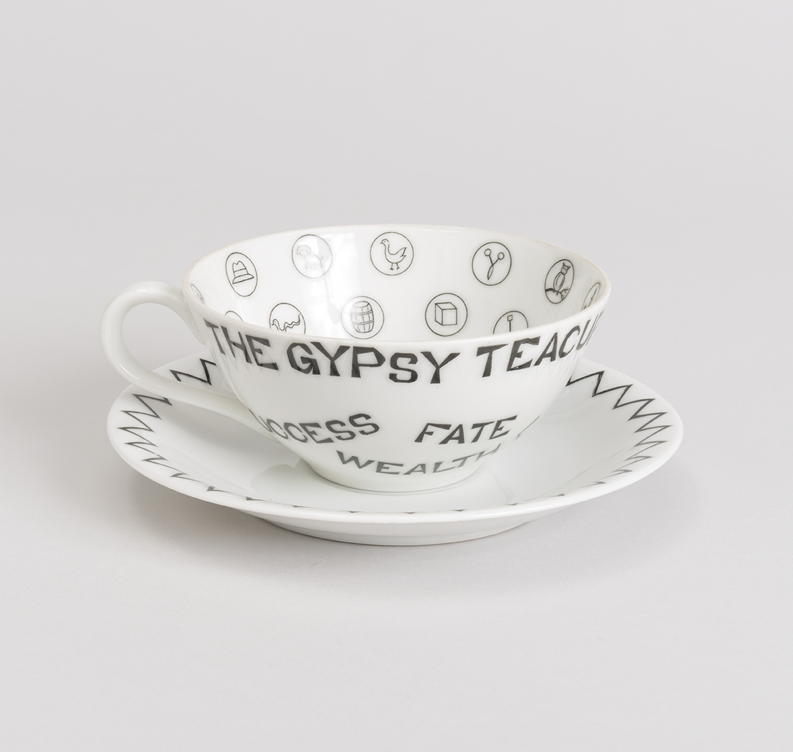 White teacup and saucer. On the exterior of the teacup are words in black such as 