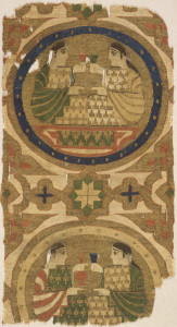 Fragment of woven silk containing one full and most of a second roundel, surrounded by interlaced bands forming star and rosette motifs. In the upper roundel, two confronted figures toast each other with cups raised; in the lower roundel the figure on the right raises a cup and the other figure a long-necked bottle. In dark blue, green, orange-red, and white on a gold metallic ground.
