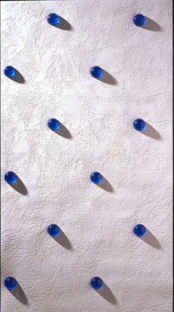 White, textured surface having the appearance of rough plaster. Has evenly spaced flat circular areas for the placement of blue glass beads, running diagonally up the sidewall.