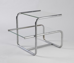 Two-tiered rectilinear form, the chromed, bent tubular metal frame with rectangular clear glass top surmounted by square clear glass shelf.