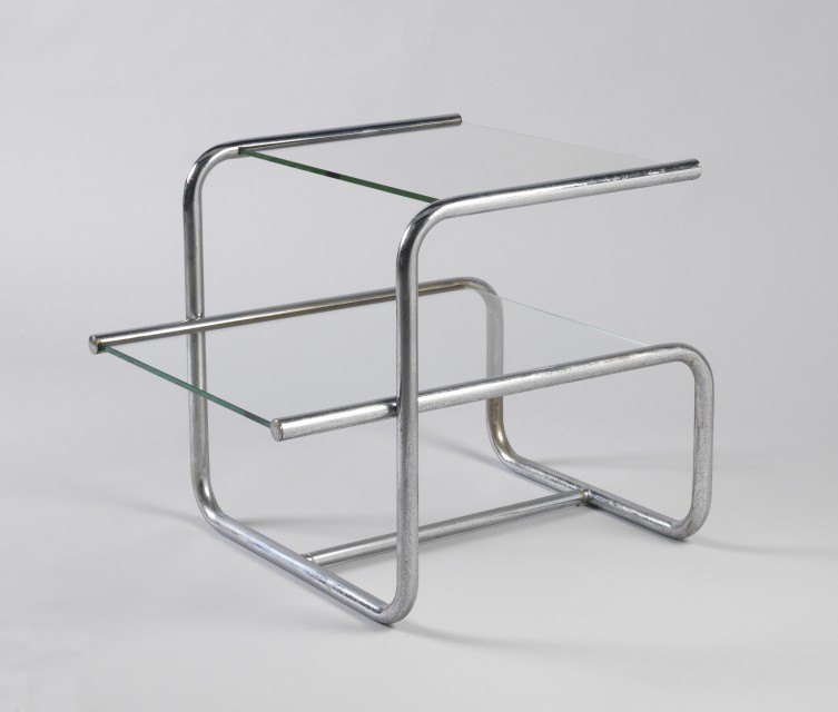 Two-tiered rectilinear form, the chromed, bent tubular metal frame with rectangular clear glass top surmounted by square clear glass shelf.