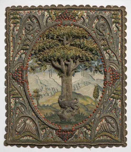 Small panel of embroidery in high relief of a tree in an oval with an elaborate framework. The field is filled by an oak tree with leaves worked in detatched needle lace stitches in shades of green. The trunk and branches are very dimensional, and are worked in silver metallic thread, now tarnished. At the base of the tree is a salamander, also in silver metallic thread. The background shows a landscape worked in pale silks with mountains and buildings, possibly a monastery. From the limbs of the tree hang crutches, a wax leg, and a censer.