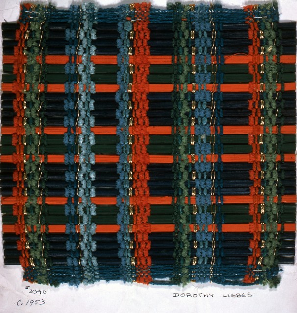 Chenille and plied yarn in red, green, blue and gold cord form even warp stripes. Weft has a repeated sequence of painted reeds: four blue, one orange, two green, and one orange.