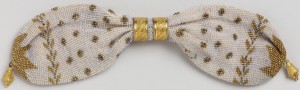 Initialed "AC" and "JC"; a base of cream-colored knitted silk is solidly covered with minute opalescent beads; it is further ornamented with gold and cut steel beads in a stylized leaf pattern and a pattern of small rosettes. Two gold rings control side opening; small gold drops at either end.