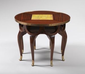 Eight-legged table with a frieze of conjoined demi-lune swags of wood under the round table top resting on the legs. The table top is centered by a square of iridescent yellow glass tiles surrounded by striated grained veneered wood panels.