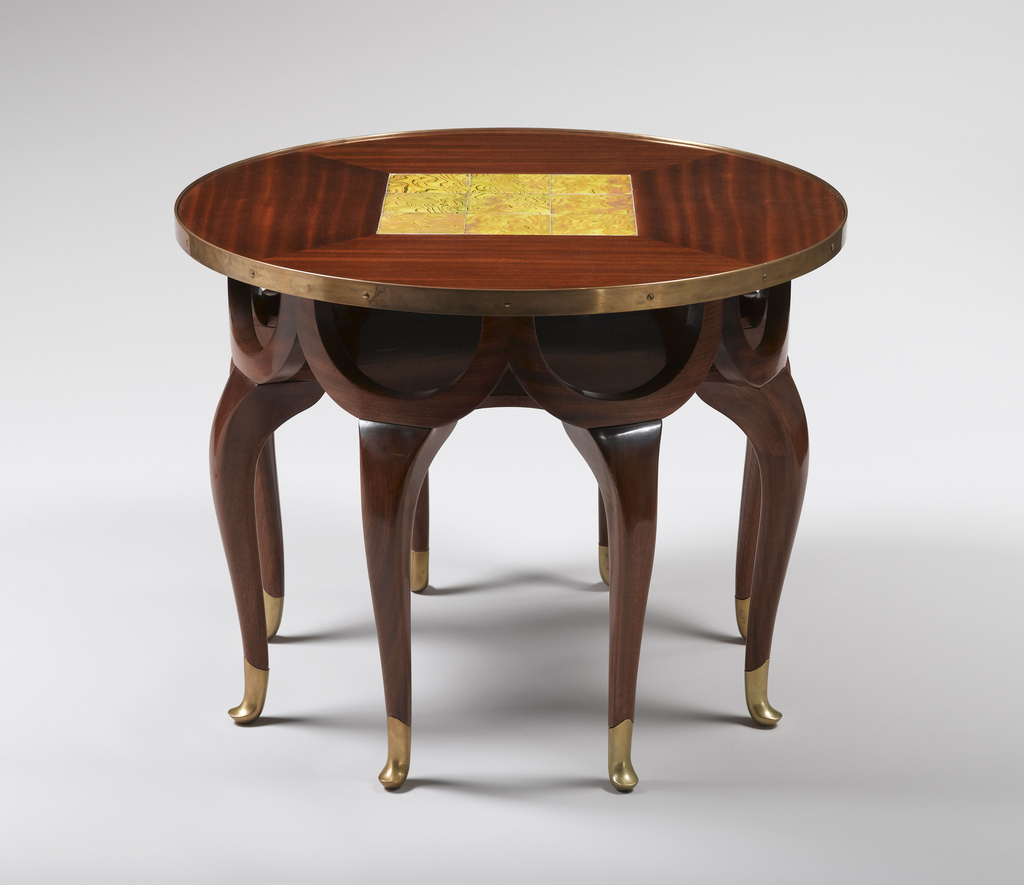 Eight-legged table with a frieze of conjoined demi-lune swags of wood under the round table top resting on the legs. The table top is centered by a square of iridescent yellow glass tiles surrounded by striated grained veneered wood panels.