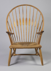 Formed as a slatted back rest fanning out with spindles that resemble peacock feathers framed by a rounded crest rail ending in a rope cord seat. The legs of the chair splay out slightly and are connected by a stretcher. Below the seat, two sticks rise up and are continued above by the arm support, where these two elements meet at an acute angle through the arm rests.