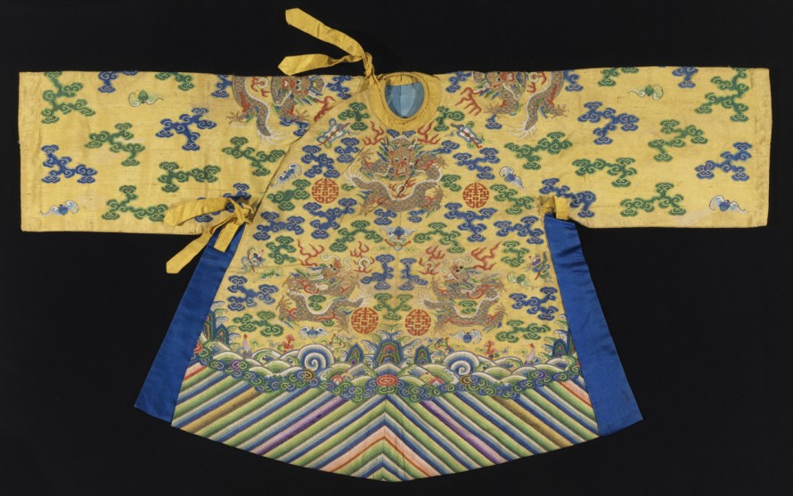 Small robe in yellow silk tapestry weave, k'ossu, with metallic gold dragons on the front, back, shoulders and sleeves. The ground is filled with clouds motifs in blue and green; flaming pearls, bats, and other auspicious symbols. At the bottom is a deep border is multicolored diagonal stripes (water convention). Assymetrical closure with yellow silk ties at the neck and side; side openings are edged with bright blue silk.