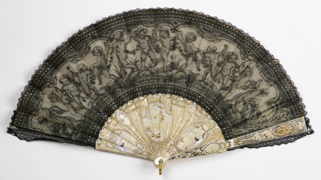 Folding fan with a black lace leaf decorated with a line of dancing putti carrying a floral garland. The sticks are carved and gilded mother-of-pearl, decorated with oval medallions of putti. On each guard stick a medallion with the initials BF.