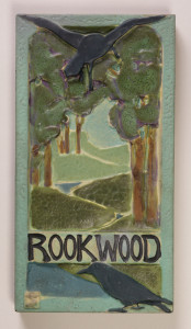Image features rectangular ceramic form showing landscape in relief featuring trees, winding river, and two ravens or rooks. Rook with outstretched wings at center top of plaque, the other perched at bottom, below the Rookwood logo. In various colored mat glazes: dark and light greens, brown, tan, pale sea-green, fuchsia and black. Border and sides in a pale sea-green. Please scroll down to read the blog post about this object.