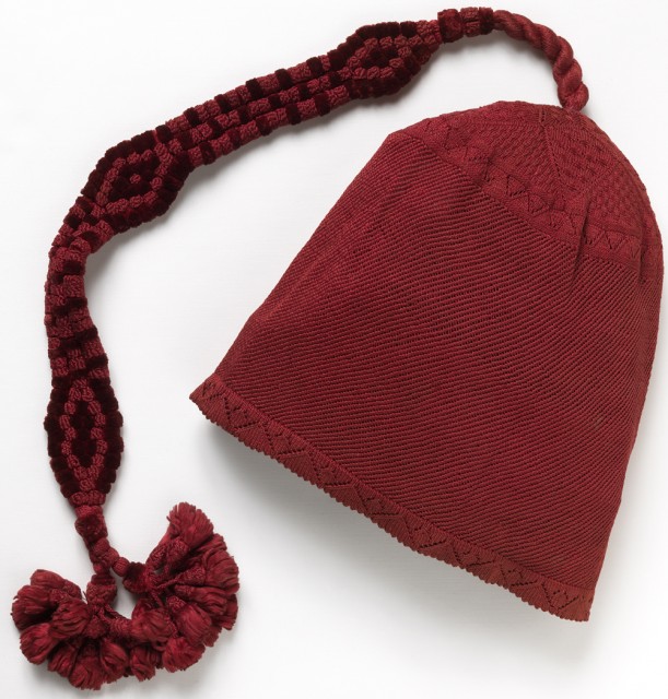 Dark red knitted silk cap with very long ornament of silk cords and chenille, forming three lozenge shapes and terminating in two tassels.