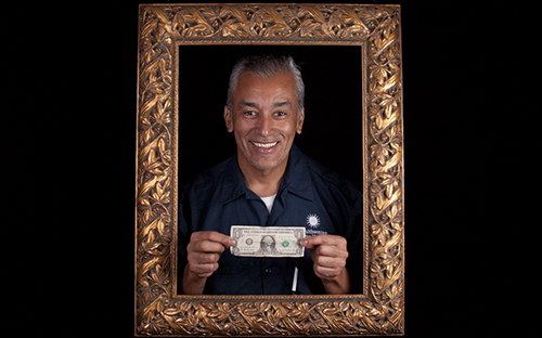 smiling man standing inside an ornate picture frame holding a dollar bill.