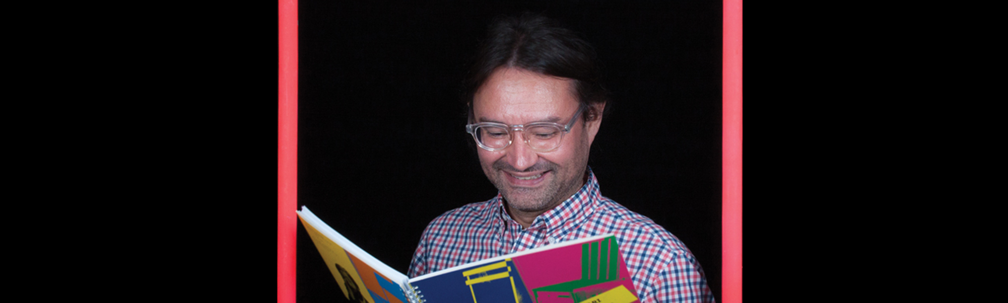 Man standing inside a picture frame reading a colorful picture book and smiling.