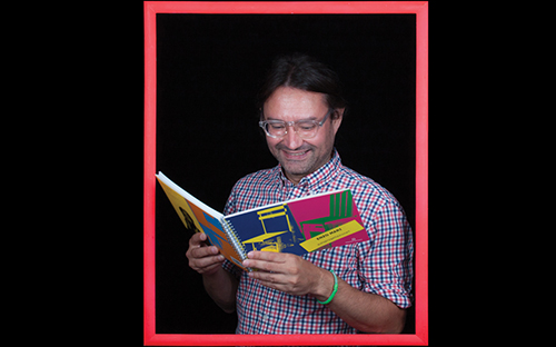 Man standing inside a picture frame reading a colorful picture book and smiling.