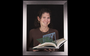 Smiling woman holding a book with colorful die-cut pages.