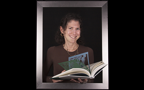 Smiling woman holding a book with colorful die-cut pages.