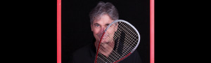 Man standing inside a picture frame holding a squash racket over one eye.