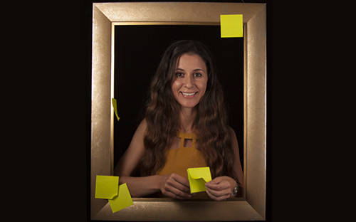 smiling woman standing inside a picture frame holding post-it notes.