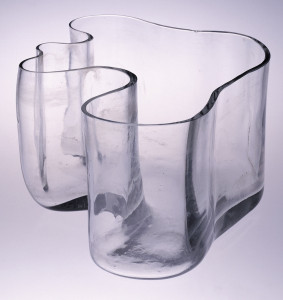 Tall, irregularly-shaped clear glass vase with flat bottom; thickness of wall varies throughout.