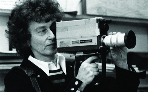 black and white photo of a young woman holding a 1980's-looking handheld camcorder.