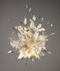 Hanging lamp composed of shards of broken white porcelain dishes, cups, saucers, serving pieces, and stainless steel cutlery, mounted on a metal frame work radiating from a central light source; the overall effect evoking an explosion of tableware.