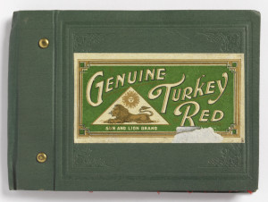 Bound manufacturer's sample book with eighteen swatches of dyed red cotton. Each swatch shows a progressive increase in density and weight of the twill woven cloth. Bound in blue leather with two brass rivets and a paper label reading Genuine Turkey Red with the logo of Sun and Lion Brand.