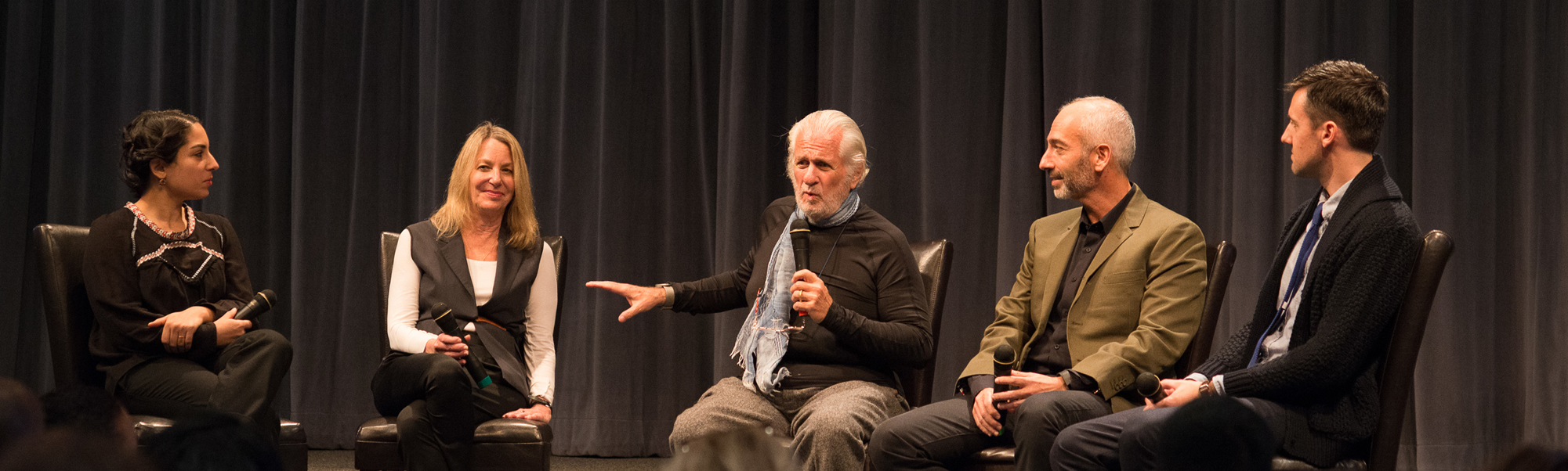 a panel of two women and three men sit on stage for a lecture