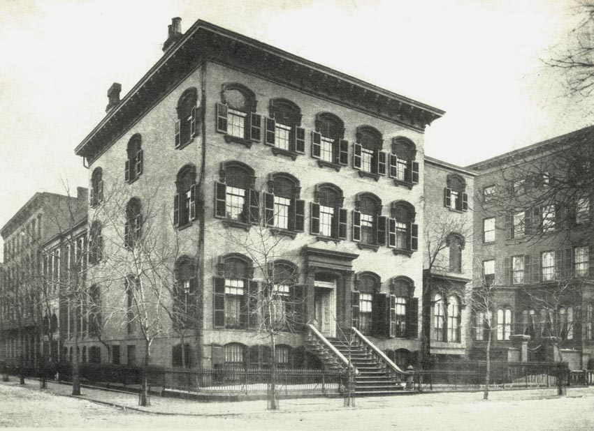 black and white photo of a three story building on the corner of a city block.