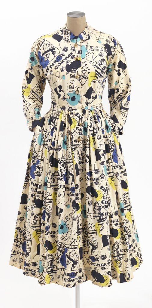 Shirtwaist dress with long sleeves and a full skirt, made from off-white printed cotton fabric with black graphic images of clowns and acrobats, with the text "J'ai seul la clef a cette parade sauvage." With patches of turquoise blue and yellow-green.