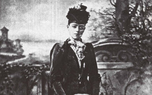 Spooky looking photo of a young woman standing outdoors in a hat and black coat.