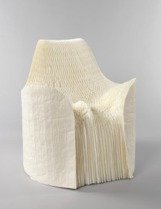 Roughly cylindrical form of thin paper layers fanned out to form chair; the front and top cut and shaped to form contoured seat, low arms, and back, the seat further compressed and contoured by designer sitting in chair.