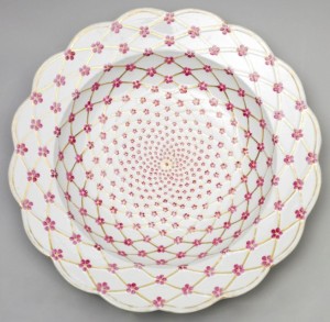 Circular form with scalloped rim; white ground decorated overall with molded and gilded trellis pattern with small pink blossoms with yellow centers at crossing points.