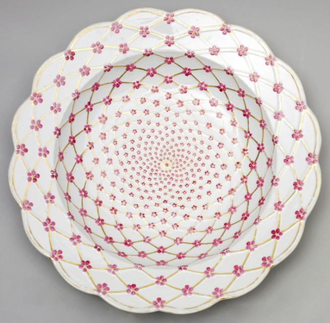 Circular form with scalloped rim; white ground decorated overall with molded and gilded trellis pattern with small pink blossoms with yellow centers at crossing points.
