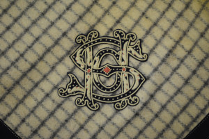 Close up of a wooly checkered blanket with large, spindly, ornate letters S H and C overlapping.