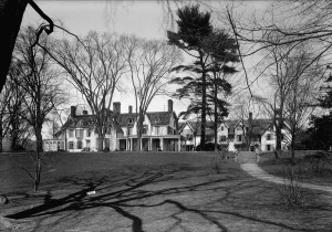 Black and white photo of a large piece of land, larger than a football field, with leafless winter trees, and a large white house with seven chimneys visible.