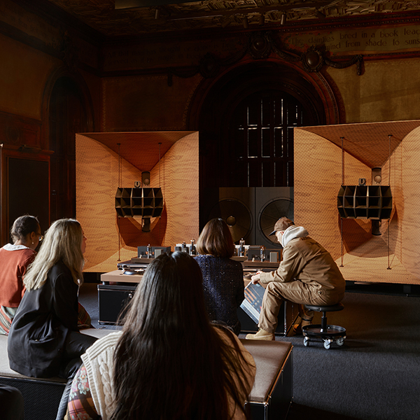 People sit together in a room with large speakers and Devon Turnbull operating a turntable setup.