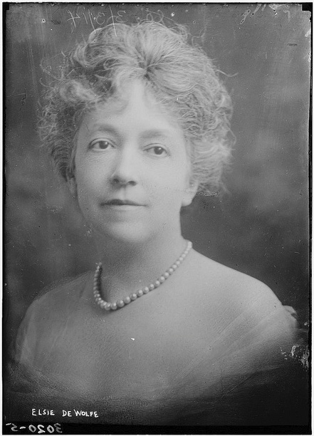 Portrait of a lady in a dress with shoulders bared, pearl necklace and curly hair swept back. Neutral facial expression looking over her left shoulder.