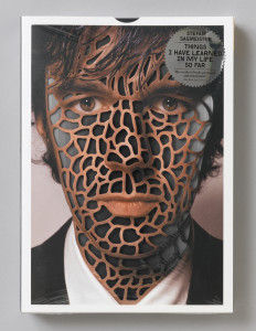 Photograph of face of man; skin covered with biomorphic trellis pattern. Upper right, starburst sticker that reads: STEFAN / SAGMEISTER / THINGS / I HAVE LEARNED / IN MY LIFE / SO FAR.