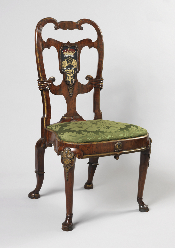 Shaped open back with voluted top rail and two horizontal crossing members enclosing a verre églomisé panel bearing the arms of the Earl of Scarsdale (extinct 1735). Cabriole sharply raking rear legs, voluted at knees, and with moulded ankles and Dutch feet. Voluted cabriole front legs with gilded pewter mounts at knees; hoof feet. Gilded pewter mask in center of front seat rail. Slip seat.