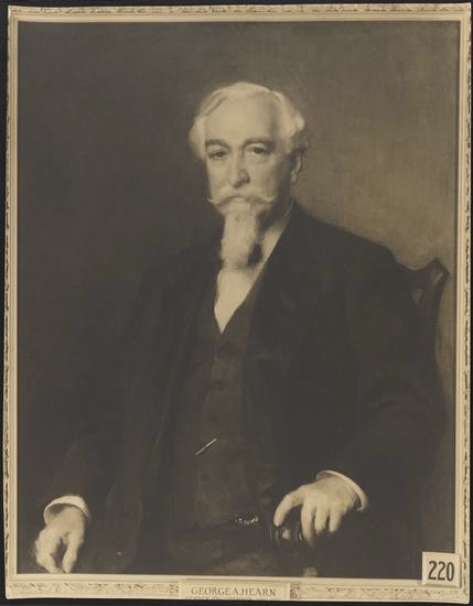 Sepia toned portrait of an older white man with white hair and long white goatee and mustache. He is seated, wearing a buttoned vest and jacket.
