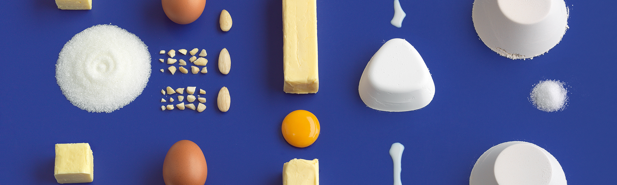 An extremely tidy array of baking ingredients laid out on a deep blue backdrop.