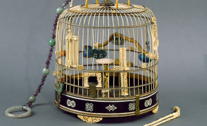 Gold birdcage with jade and amethyst string of beads coming from the top and fancy bird toys and perches inside.