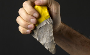 Image of a young man's fist holding a carved stone arrowhead with handle side tipped with bright yellow silicone.