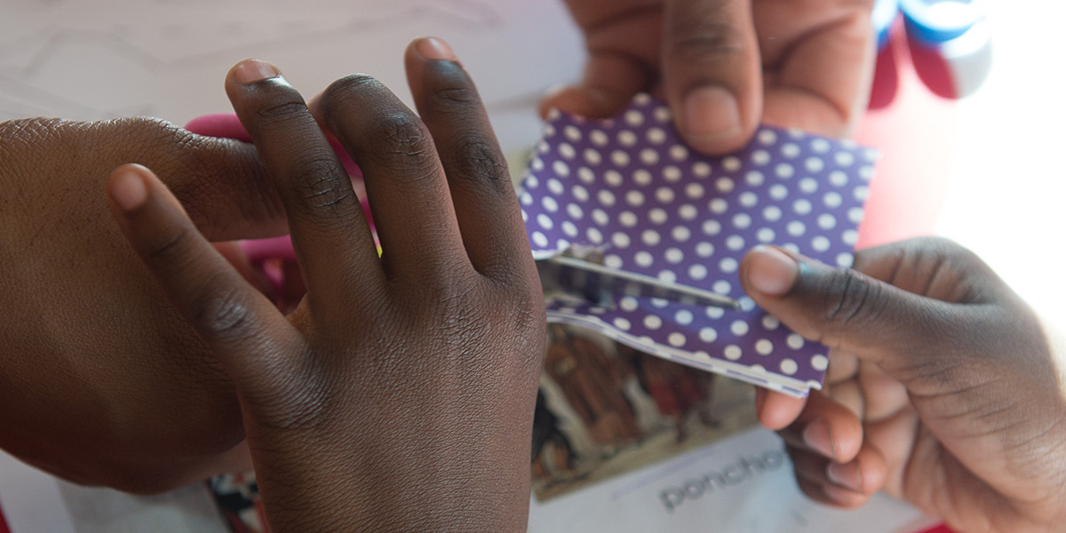 two pairs of hands, what appears to be a mother and small child, handling bits of colorful paper, as if collaborating on an art project