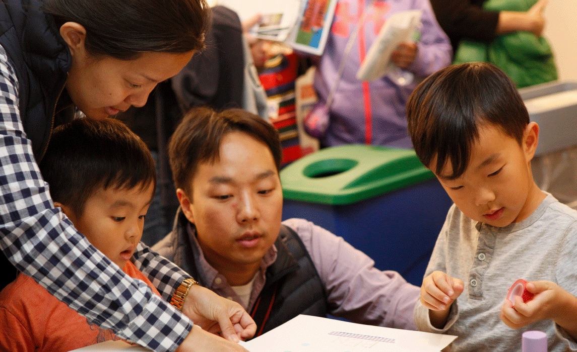 A man and a woman help two young children with an activity at a table.