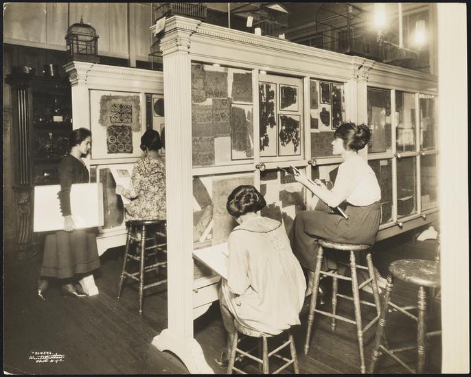 Women on stools studing items in cases and taking notes