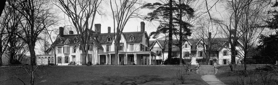 Black and white photo of a large piece of land, larger than a football field, with leafless winter trees, and a large white house with seven chimneys visible.