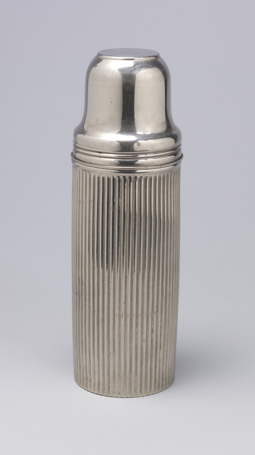 Cylindrical, fluted metal body, horizontal ridges at top; tapering, flat-topped, cylindrical metal cup inverted over bottle mouth to serve as cap; cap unscrews and lifts off to reveal small cylindrical rubber stopper, with circular metal top and hinged toggle latch, set snugly into circular mouth of interior glass vacuum bottle.