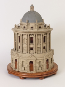 the circular building with rusticated lower tier supporting set back upper tier with double columns between window bays, alternating blind and paned windows, surmounted by a domed top with finials around and a spire above, all replicating the Radcliffe Camera building in Oxford England.